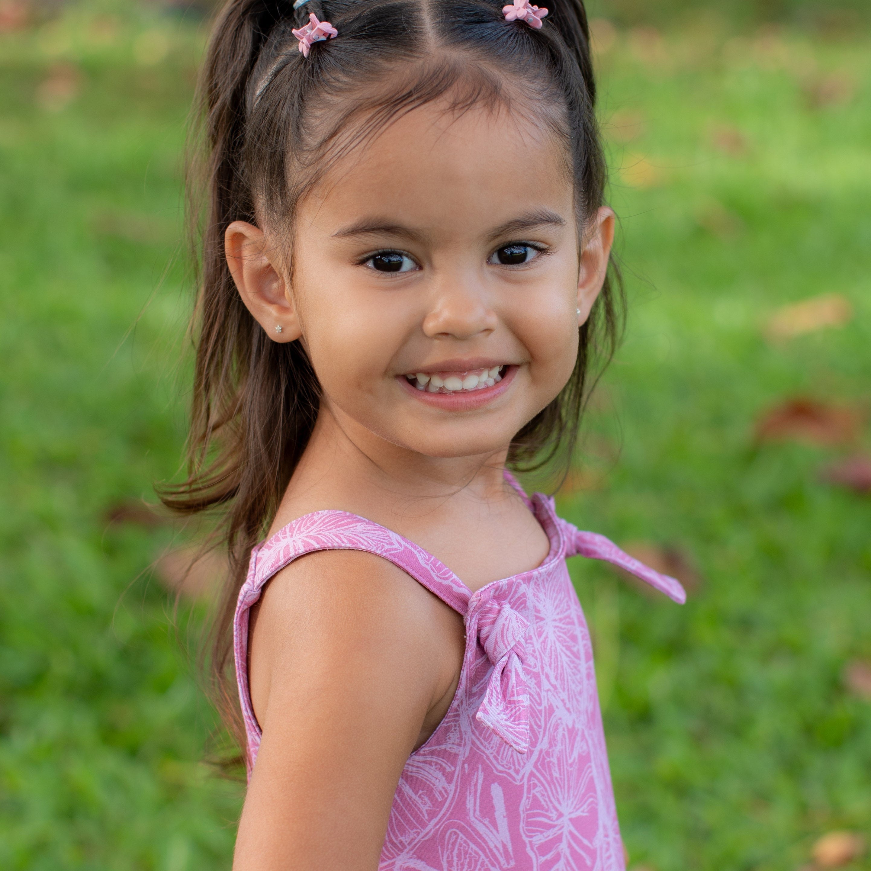 toddler girl in a pink overall romper standing on grass