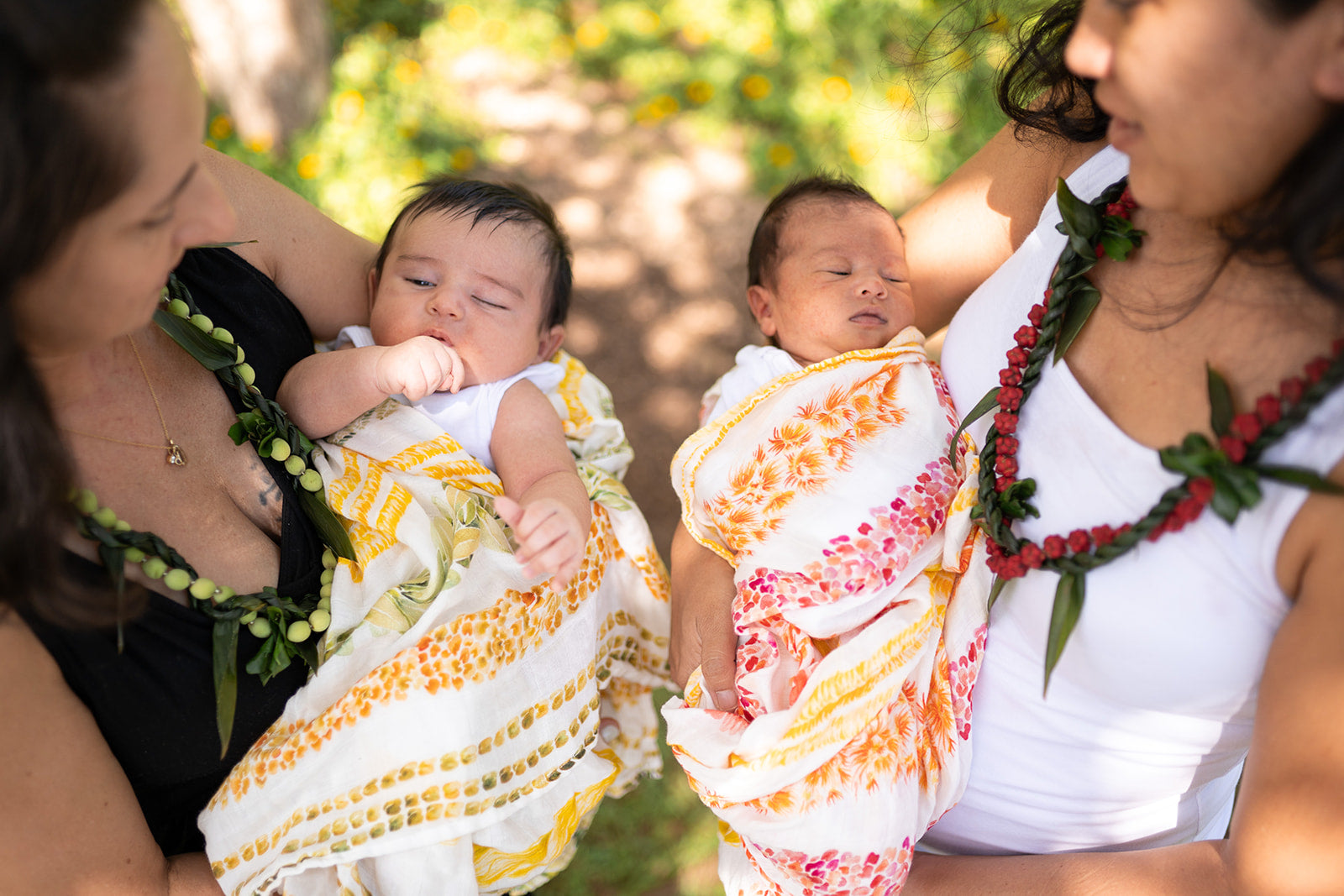 two babies held by their moms and swaddled in lei alaula prints