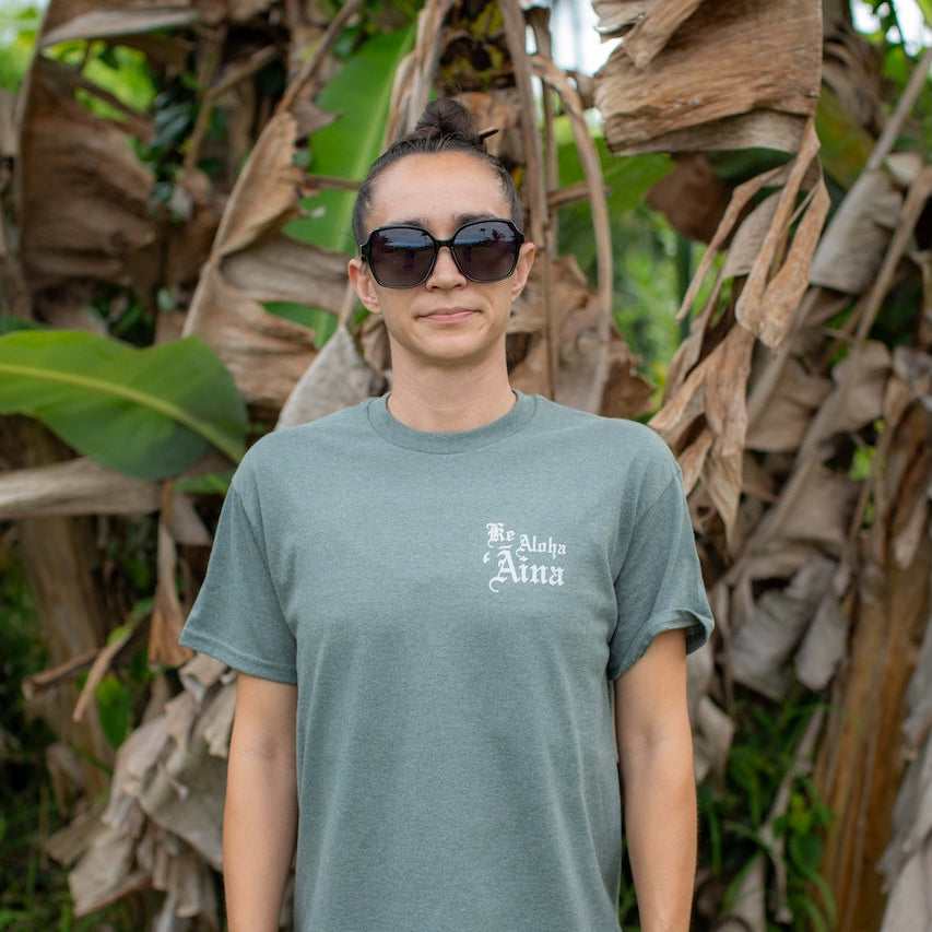 Person wearing a green t-shirt with text in front of leafy plants
