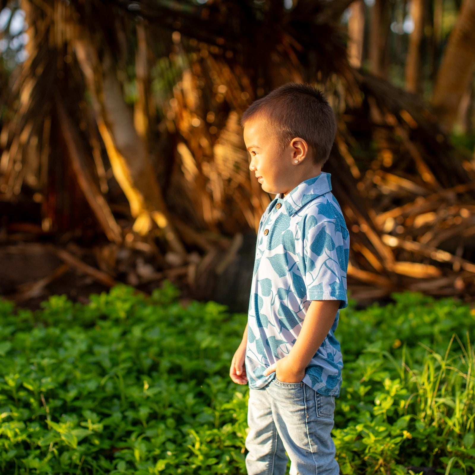 Young boy standing in a grassy area with large trees in the background