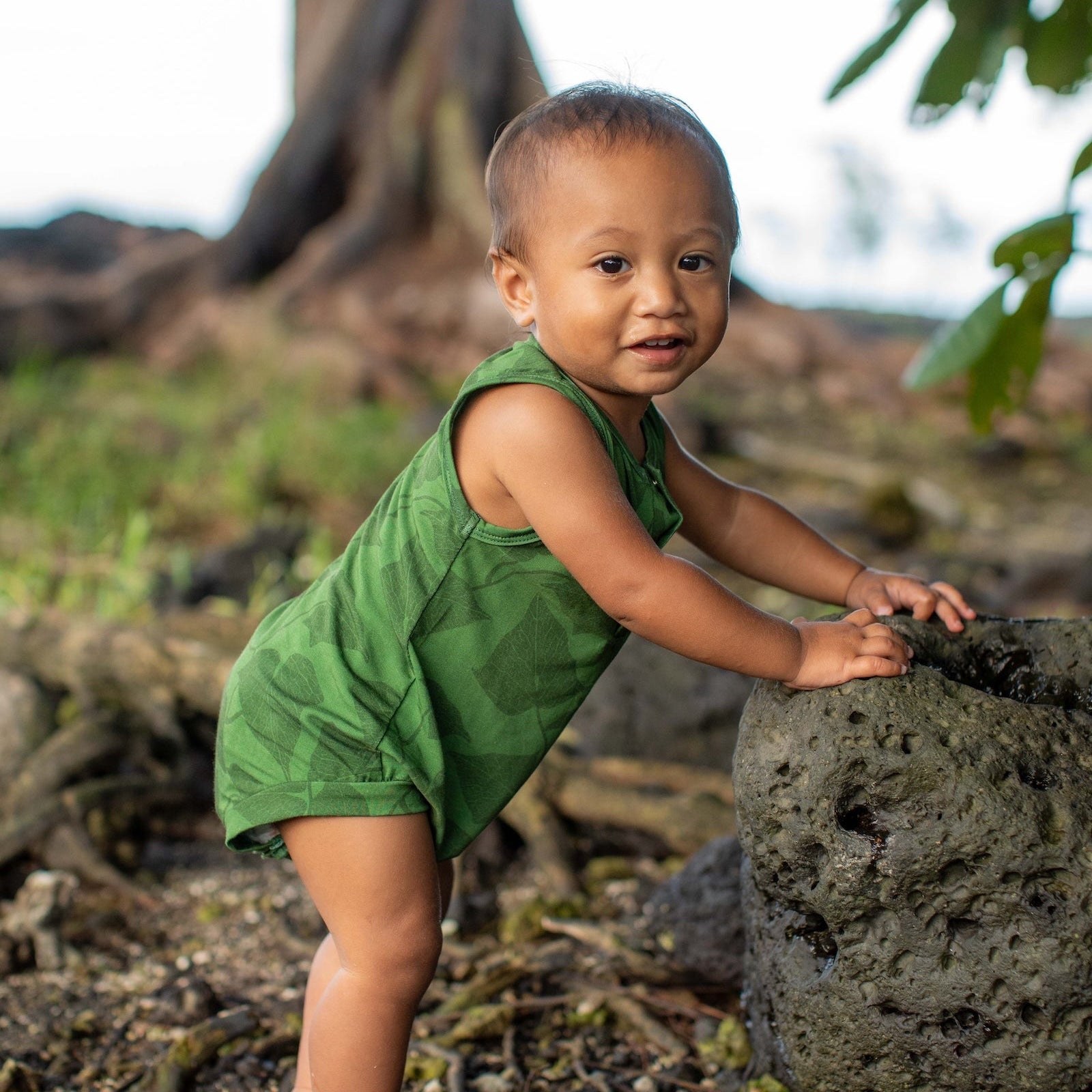 Child in a green outfit standing on a rocky ground with trees in the background