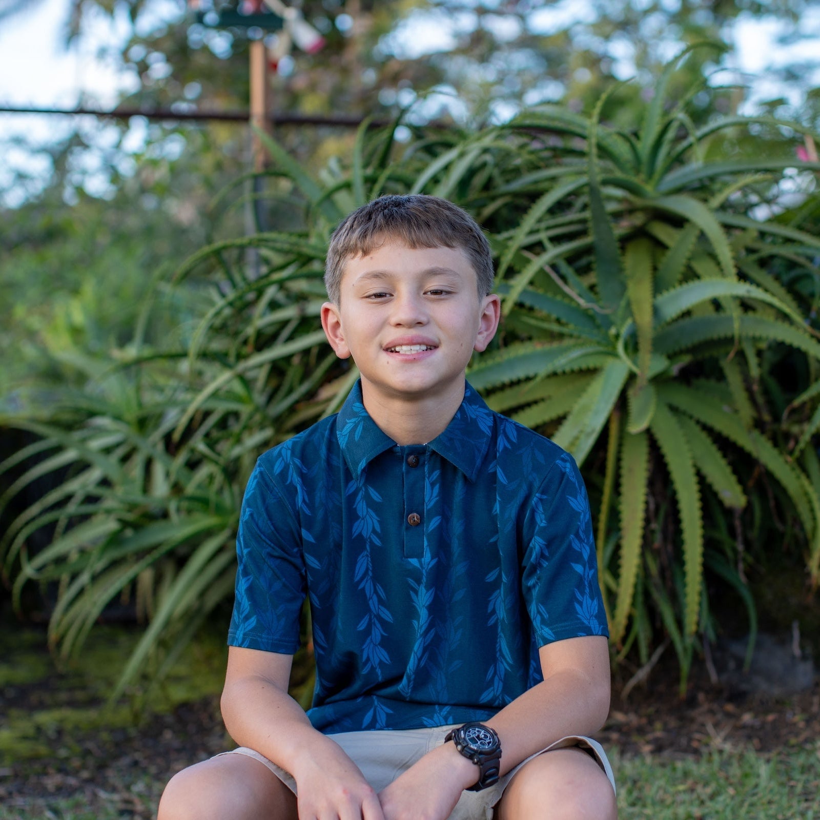 Young boy sitting outdoors with green plants in the background