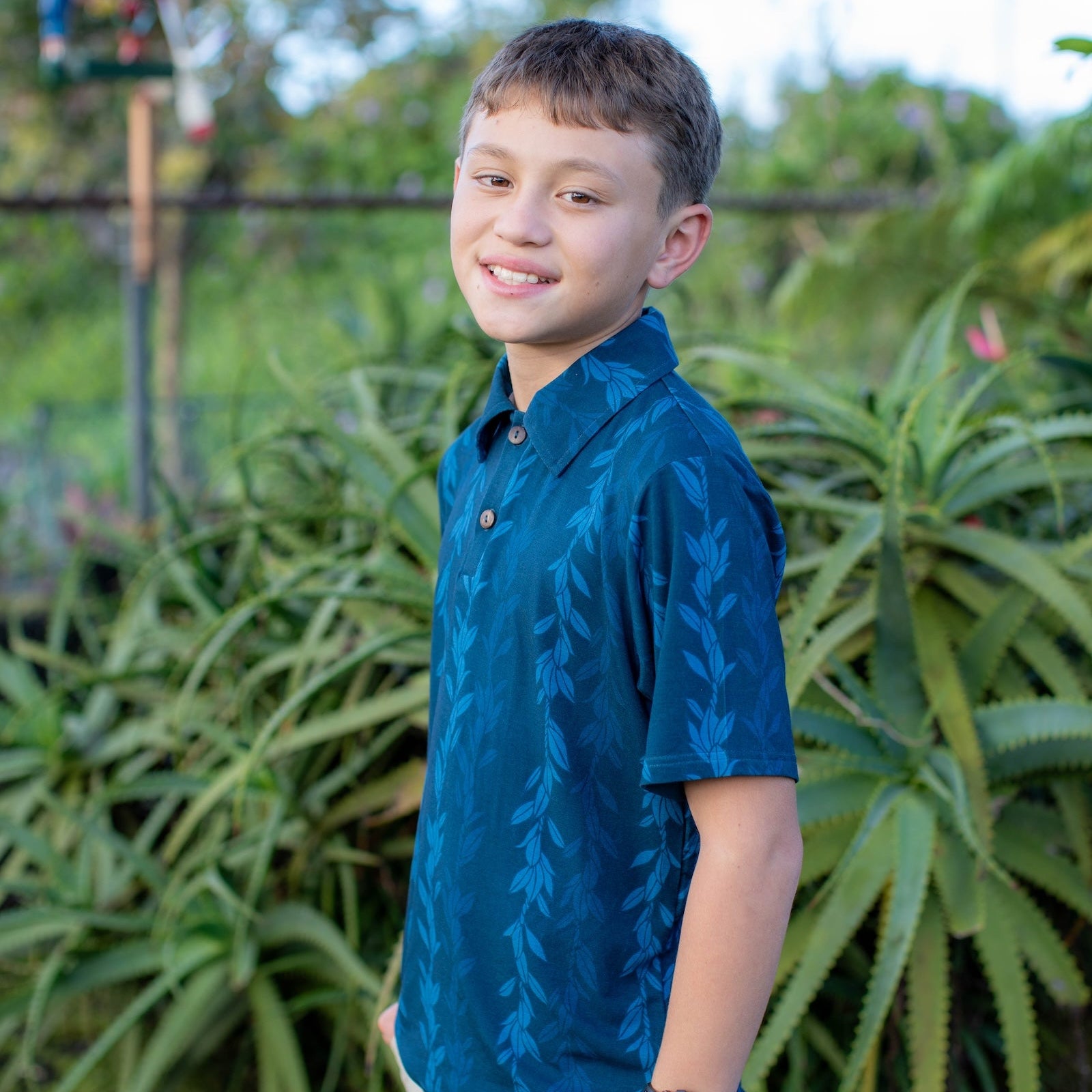 Young boy in a blue shirt standing in front of green plants