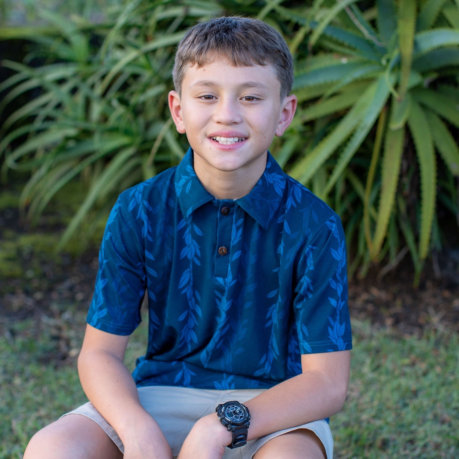 Young boy sitting outdoors with green plants in the background
