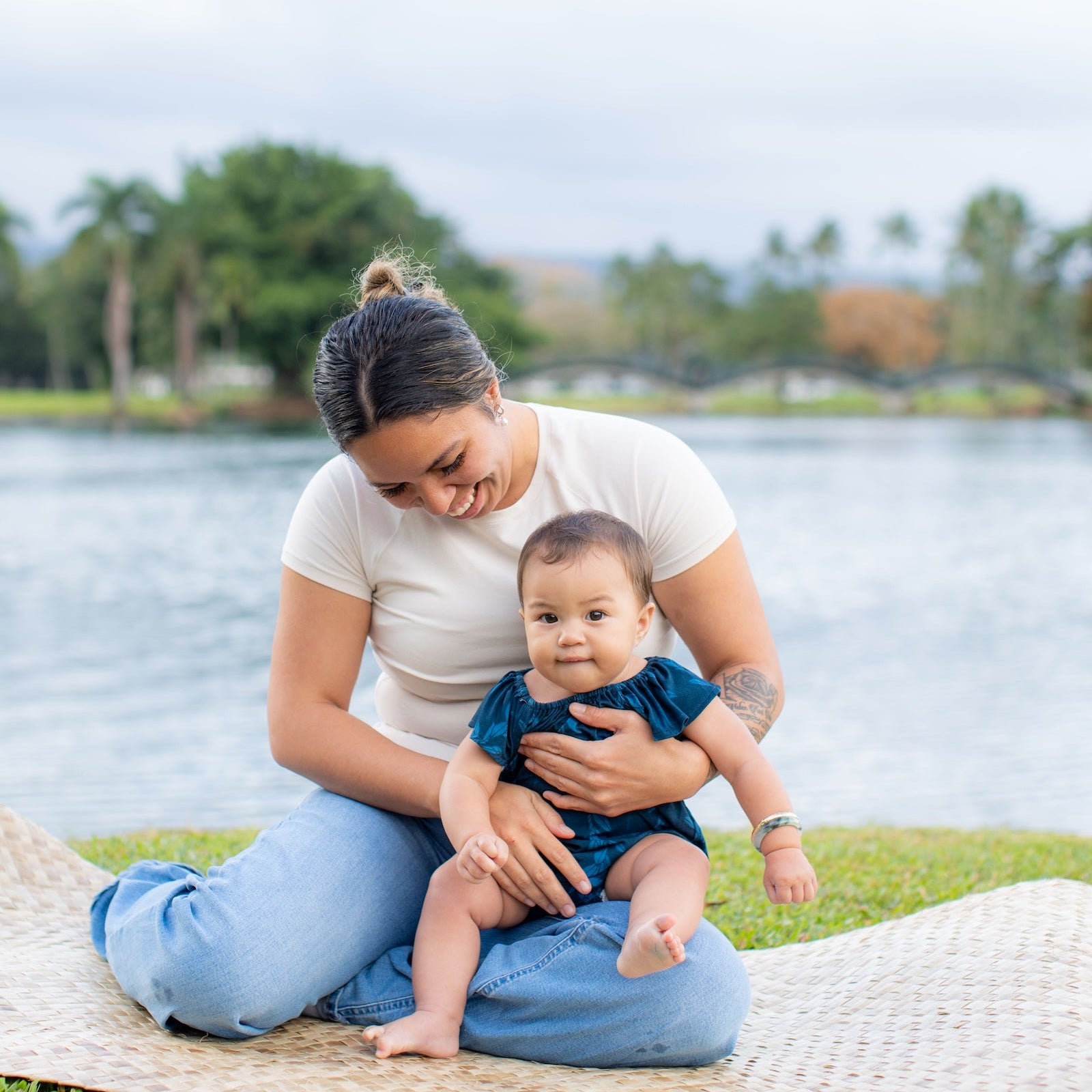 Woman holding a baby on a grassy area by the water