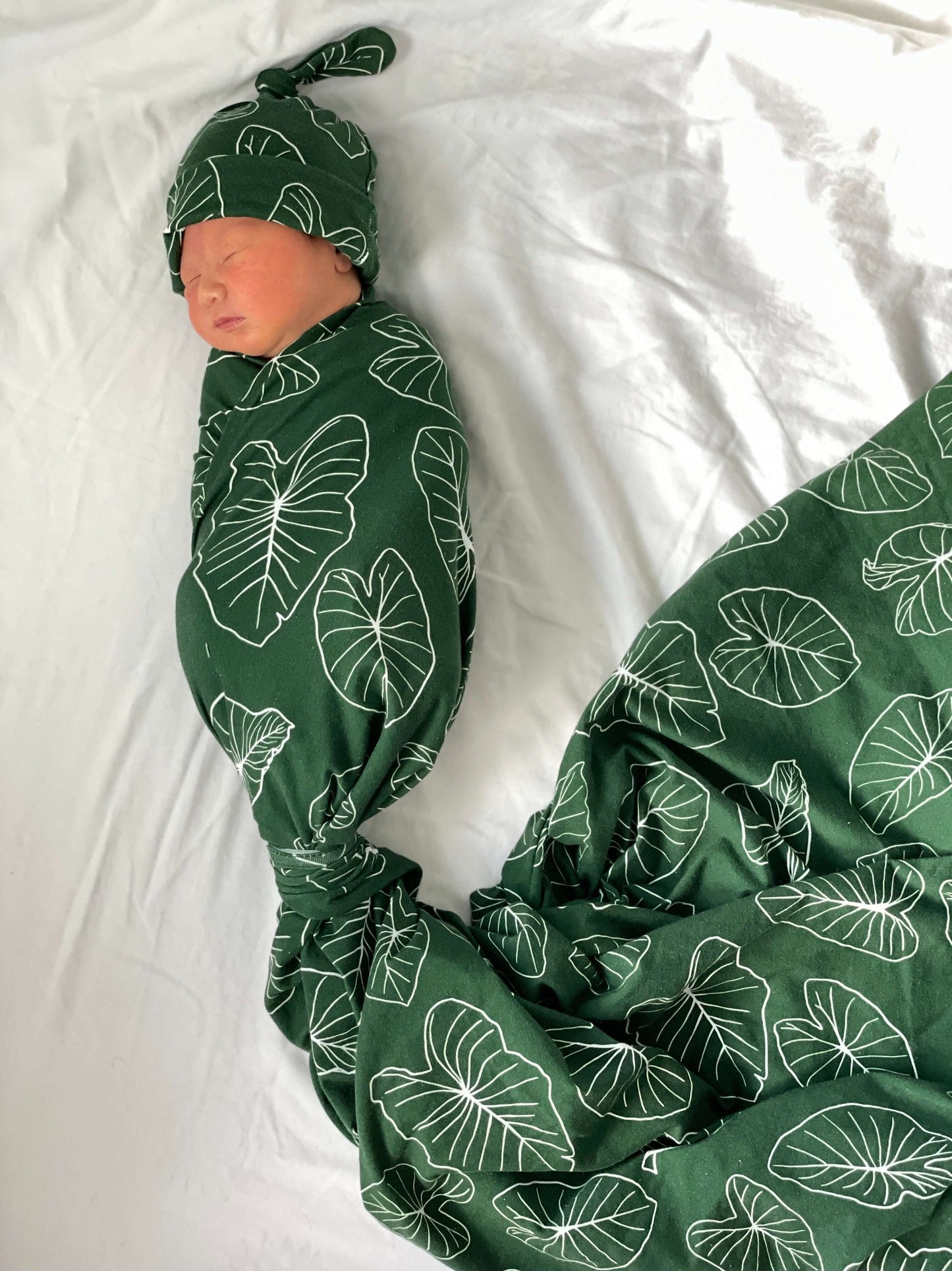 newborn baby wrapped up in the hawaiian kalo jersey blanket and wearing the newborn knot beanie from the keiki dept