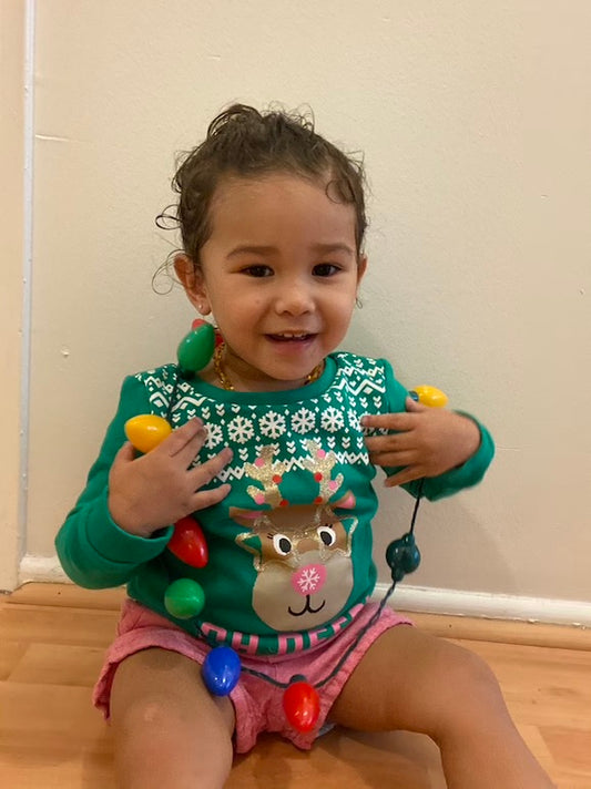 toddler wearing ugly christmas sweater and christmas light necklace