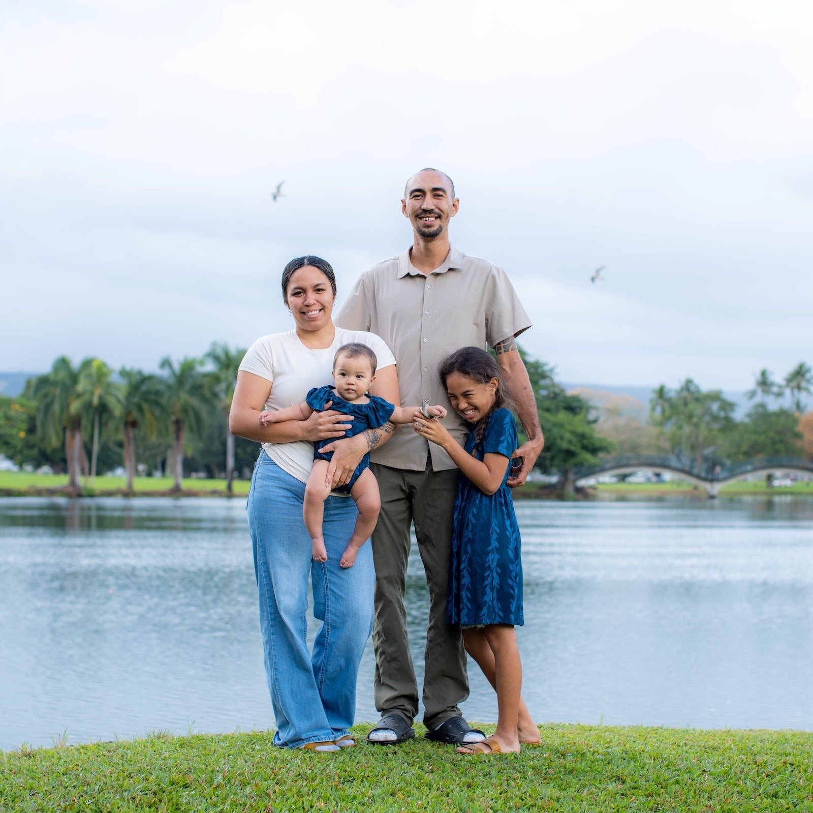 Family of four standing on grass by the water with trees in the background