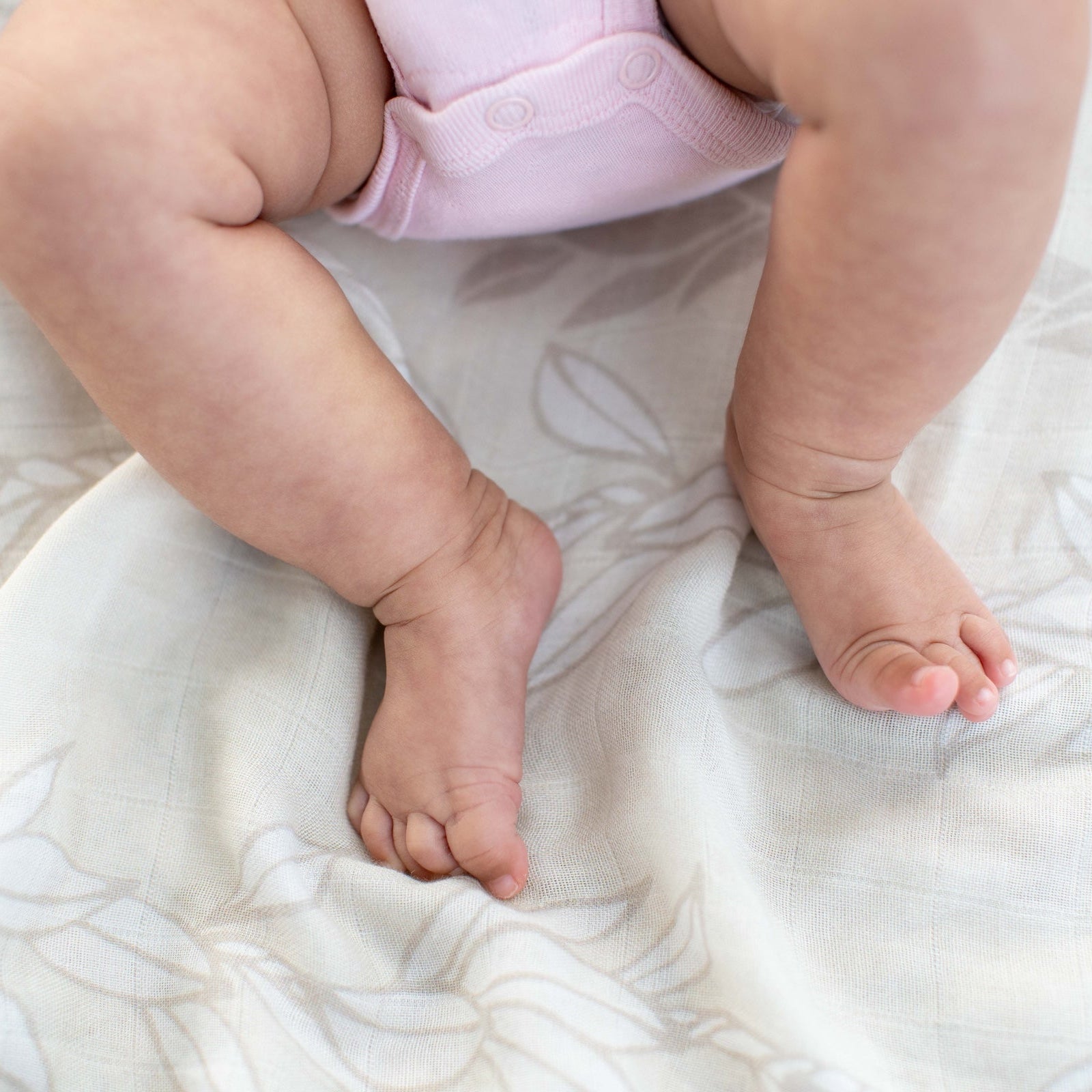 Baby's feet and legs in a pink diaper on a ivory white maile strands pattern blanket