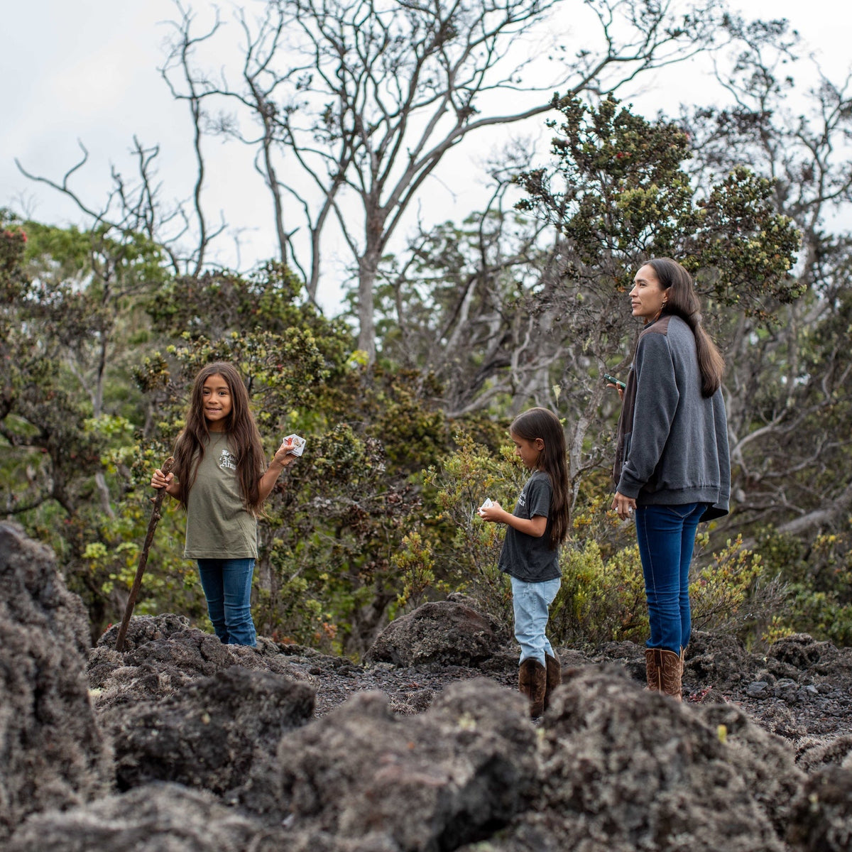 Three people walking through a forested area with rocky ground