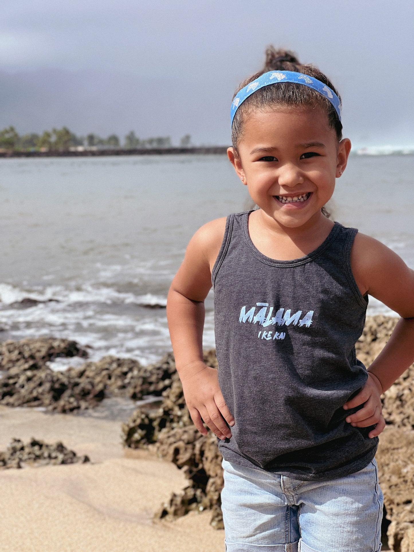 young girl wearing a malama i ke kai tank top. she is standing on the shoreline