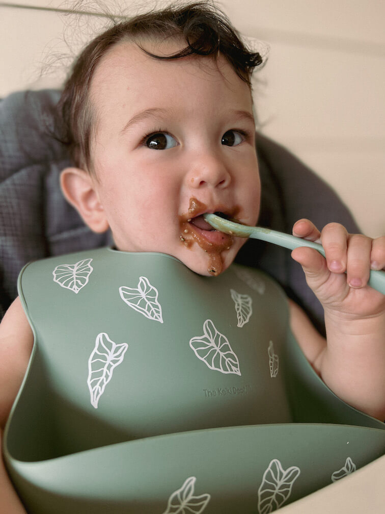 baby feeding himself while wearing the kalo silicone bib from the keiki dept