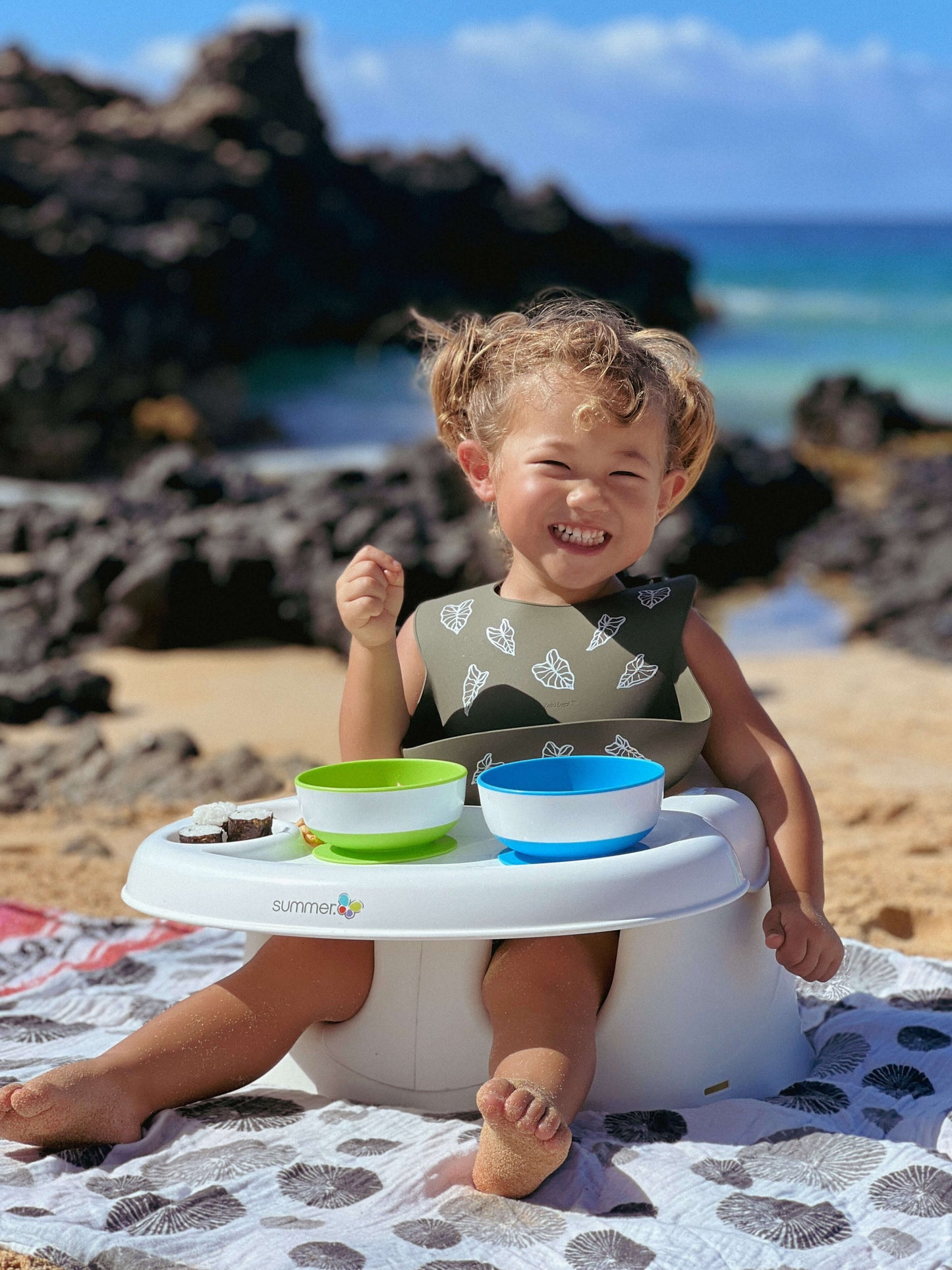 toddler girl eating at the beach using kalo silicone bib from the keiki dept